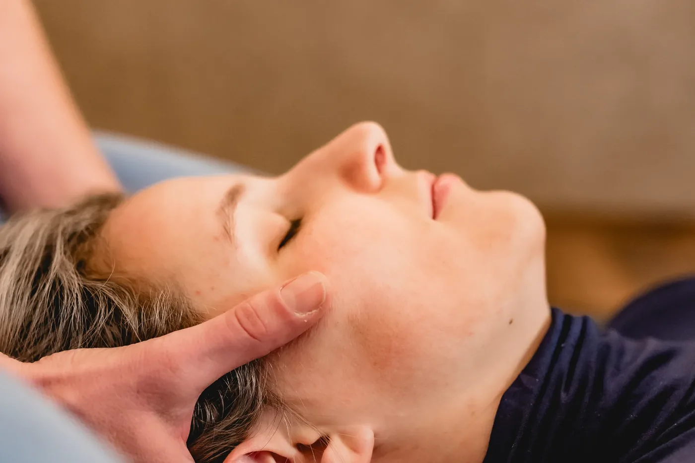 Nahaufnahme einer Shiatsu-Behandlung: sanfter Druck an Kopf und Schläfen einer entspannten Klientin